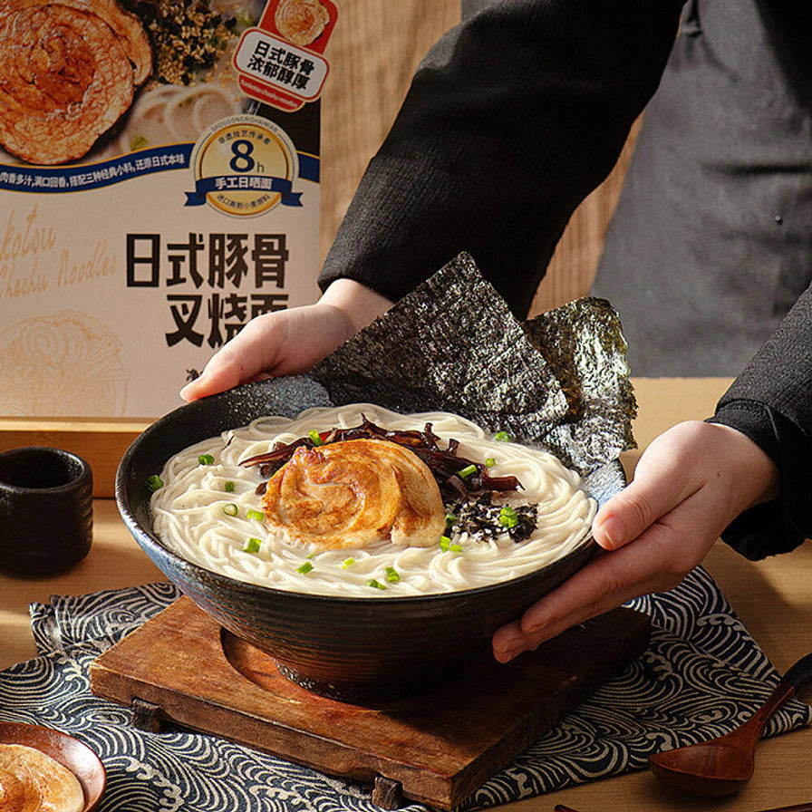 双手端着一碗热腾腾的日式豚骨叉烧面，碗中可见大片叉烧、海苔和葱花。
