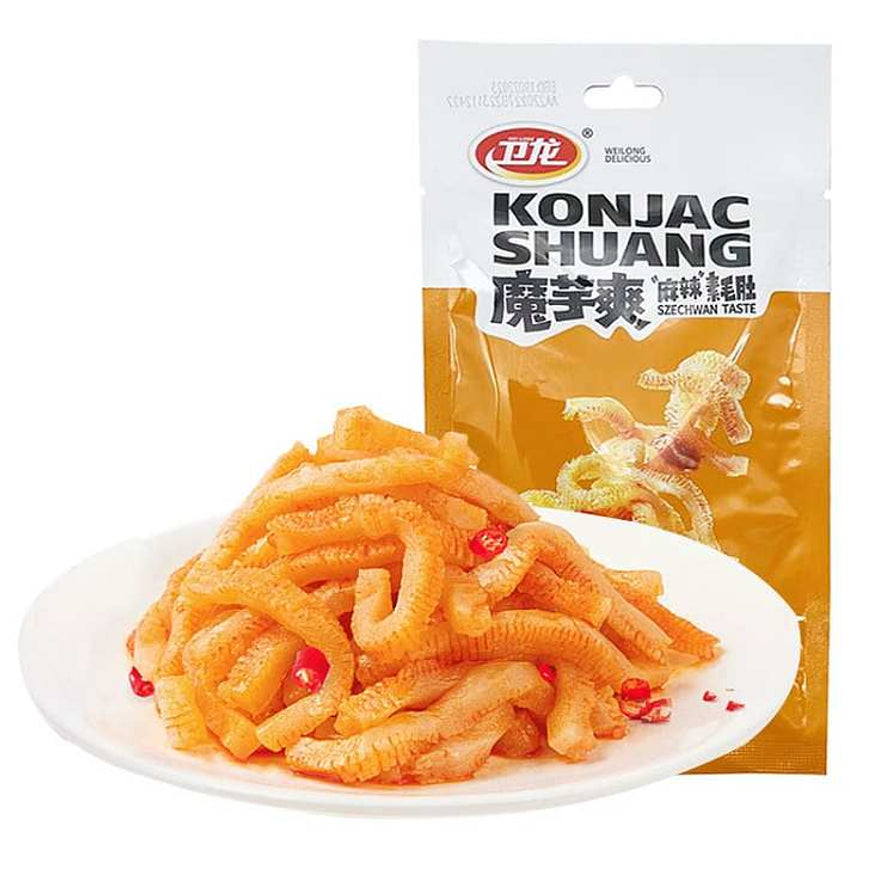卫龙魔芋爽麻辣味素毛肚橙色包装，特写镜头展示白瓷盘中堆叠的麻辣魔芋丝，点缀有碎辣椒。