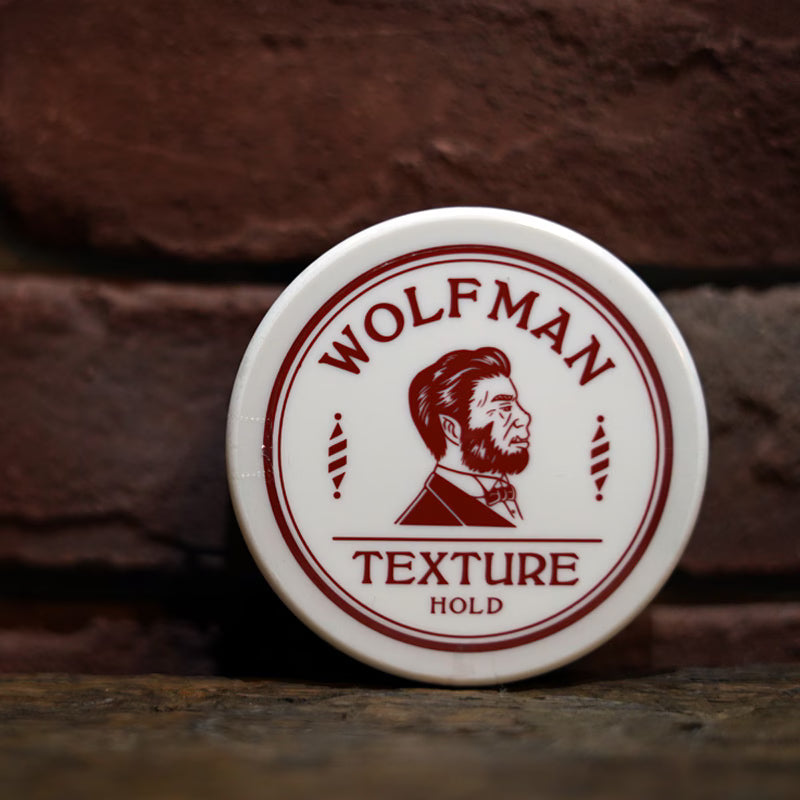 Wolfman 造型发油放置在深色砖墙前的木质台面上，展示产品包装与环境氛围。