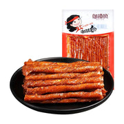 邬辣妈麻辣豆卷，黑色圆盘中整齐叠放着数条裹满红油和辣椒碎的紧实豆卷，背景为红白配色的商品包装袋。