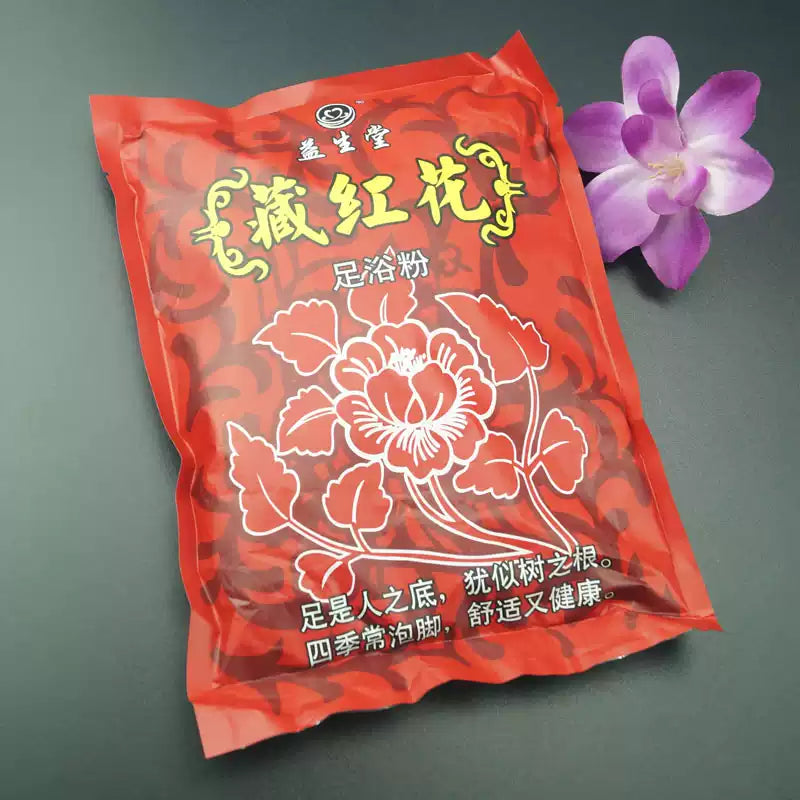 益生堂藏红花足浴粉红色包装袋正面，印有品牌名、产品名及花卉图案，旁置一朵紫色鲜花。