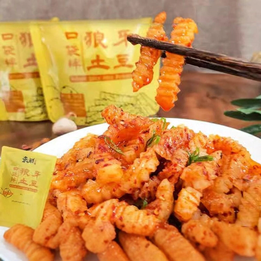 盘中盛放着裹满红油辣椒的波浪形狼牙土豆，筷子夹起一块展示其脆爽质感，背景为产品包装袋。