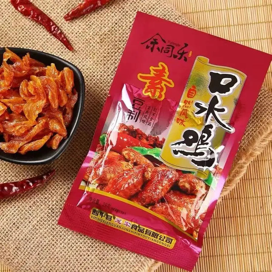 余同乐口水鸡包装袋斜放在草席背景上，旁边配有一小碟麻辣素肉和干辣椒装饰。
