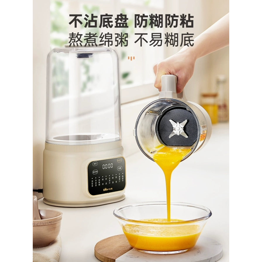 正在倾倒南瓜浓汤的小熊破壁机，展示不粘底盘和防糊防粘特性，背景为厨房环境。