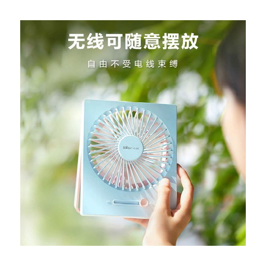 手持小熊桌面风扇的特写，背景为户外绿植，上方带有“无线可随意摆放”的中文说明文字。
