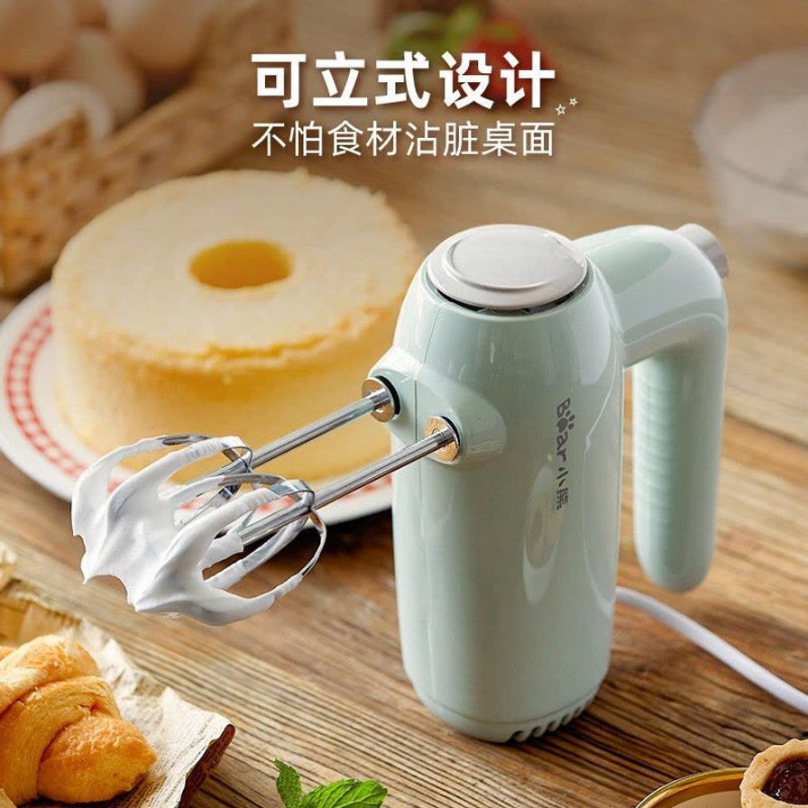 小熊电动打蛋器正在打发奶油，可立式设计展示，背景有戚风蛋糕和烘焙食材，上方配有“可立式设计”中文说明。