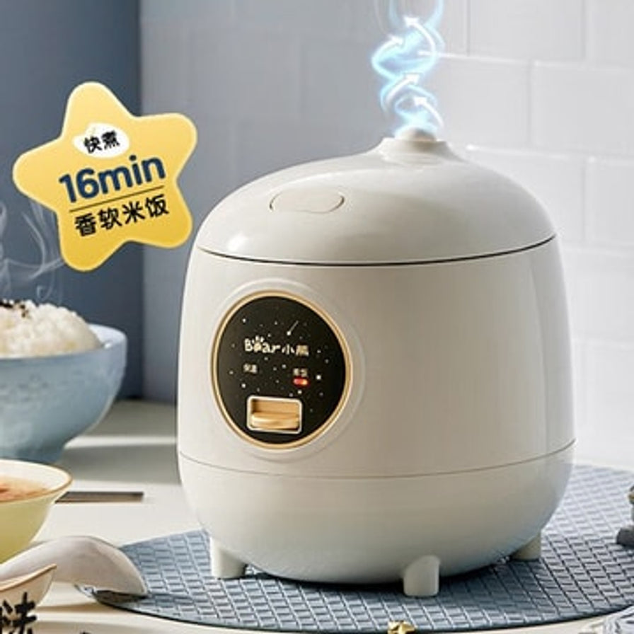 小熊迷你电饭煲放置在餐桌上，顶部冒着蒸汽，左侧有黄色星形角标写着16分钟快煮香软米饭。