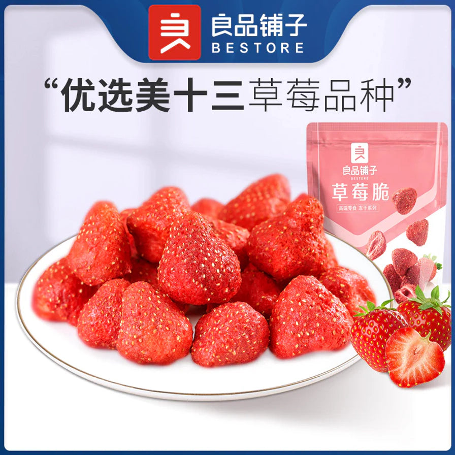 白色圆盘中堆叠的整颗红色冻干草莓，背景包含良品铺子品牌标识、产品包装袋及新鲜草莓，上方有“优选美十三草莓品种”字样。