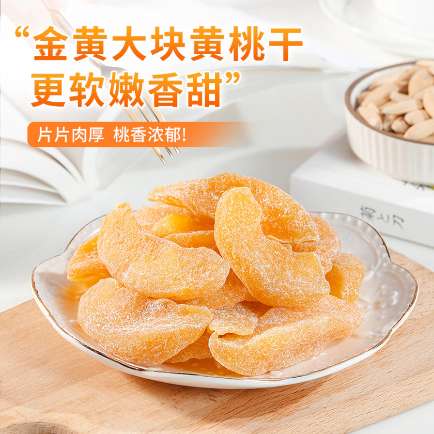 盛放在白色瓷盘中的大块黄桃干，背景有书本和木质托盘，上方配有金黄大块黄桃干更软嫩香甜的文字。