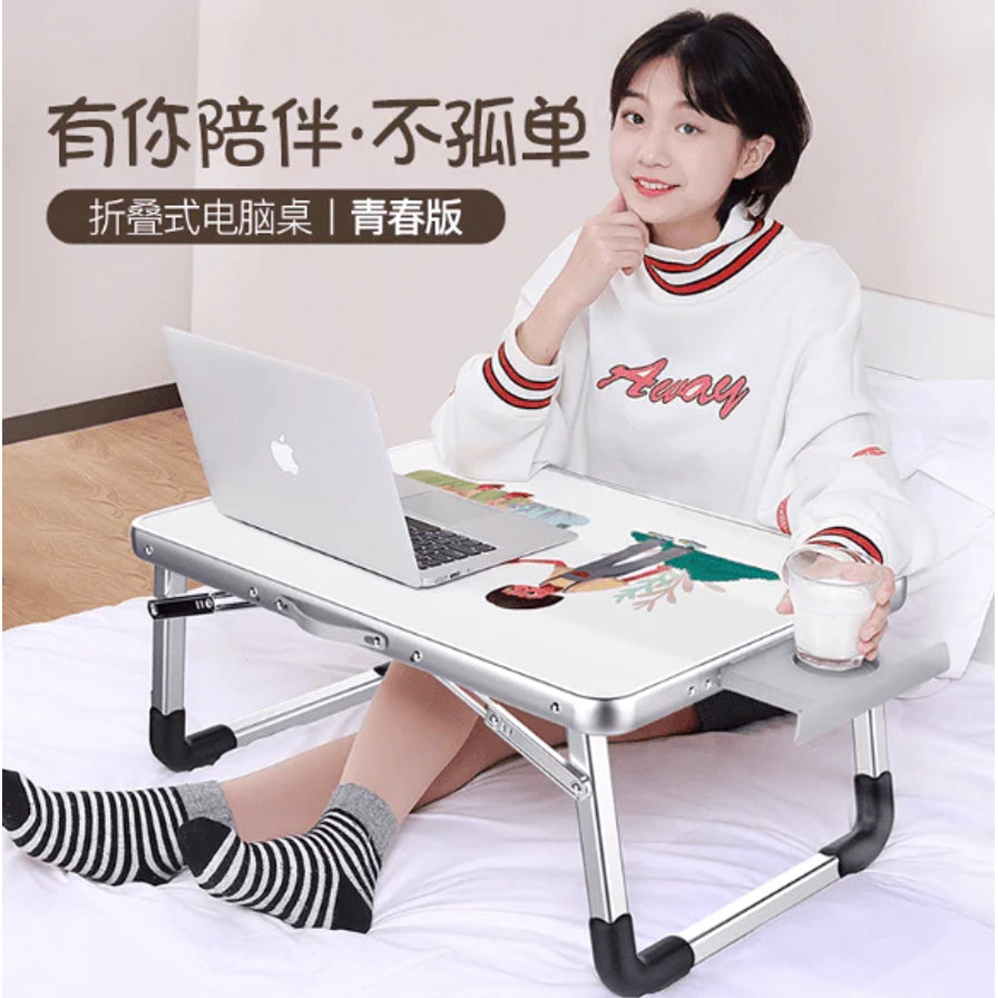 女生坐在床上使用折叠电脑桌，画面左上有“有你陪伴·不孤单”和“折叠式电脑桌 | 青春版”文字