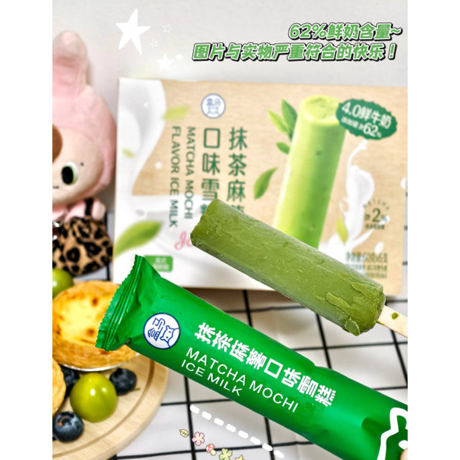 手持一支拆封后的盒马抹茶麻薯雪糕，背景为产品包装盒和绿色独立包装袋，上方带有62%鲜奶含量的中文卖点文字。