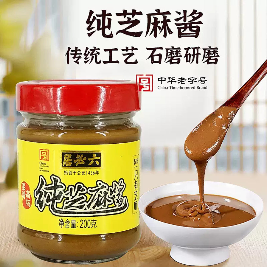 六必居纯芝麻酱展示，背景带有传统工艺石磨研磨字样，勺子正从碗中舀起质地细腻顺滑的芝麻酱。