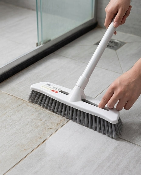 长柄地板刷清洁浴室瓷砖缝隙的场景示意图，展示不弯腰站立操作和硬毛刷头去污细节。