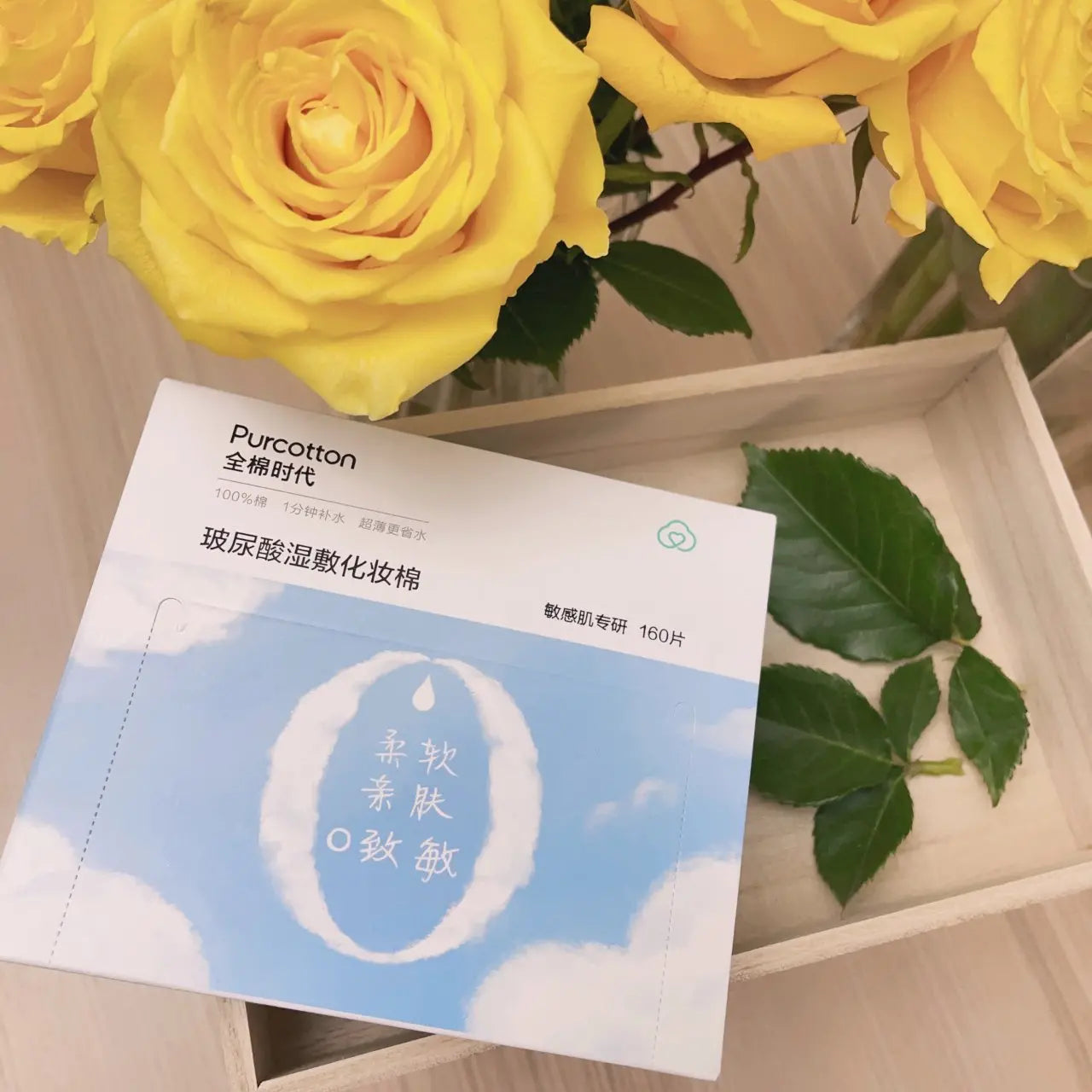 全棉时代化妆棉放置在木盒中，背景有黄色玫瑰花装饰的生活场景图。