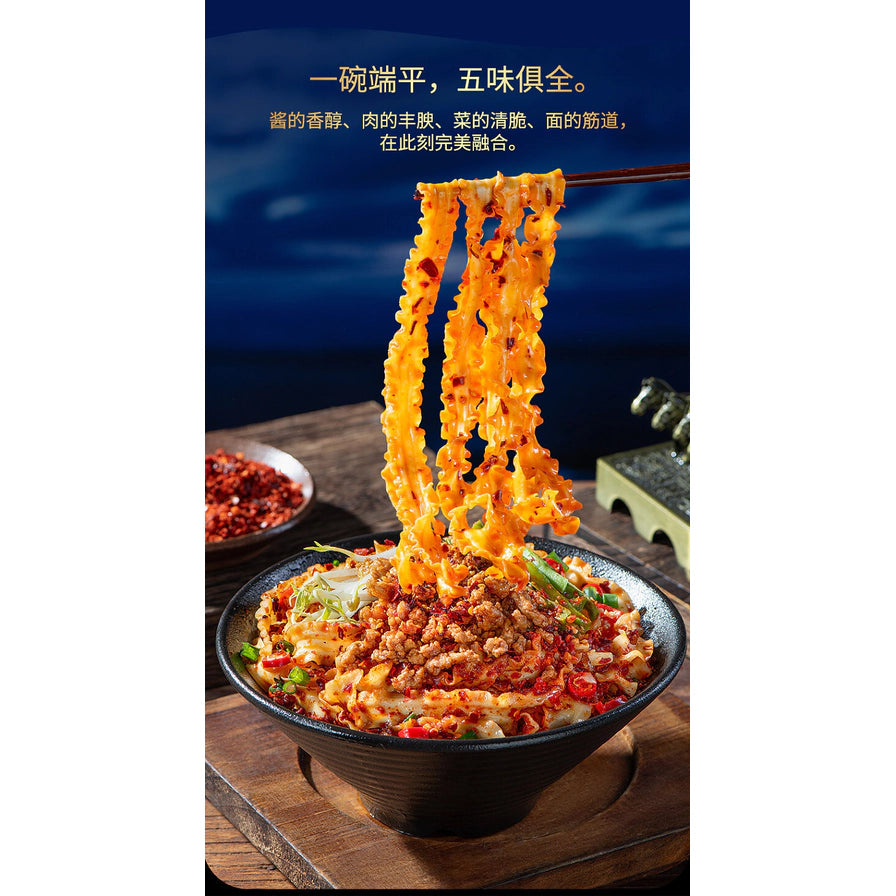 用筷子挑起宽大劲道的波浪形面条，面条裹满红油酱汁，背景为一碗完整的拌面。