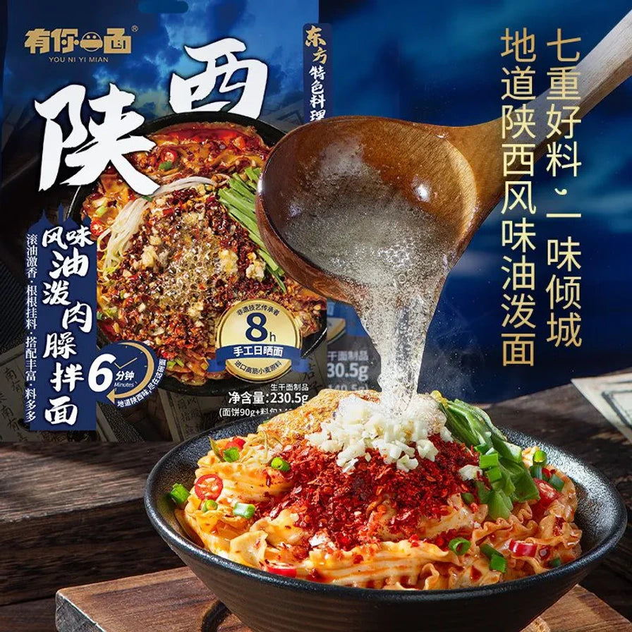 木勺向碗中的面条浇淋热油，碗中配有红辣椒粉、蒜末和葱花，背景带有地道陕西风味宣传文字。