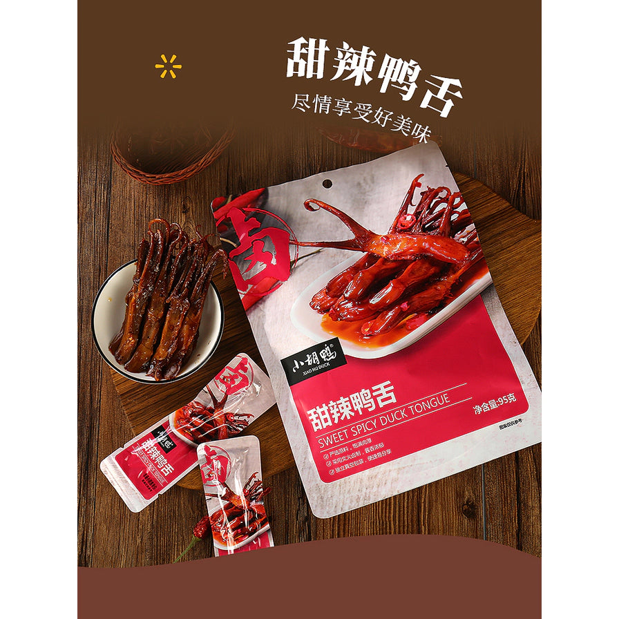 木质背景上的小胡鸭甜辣鸭舌，包含大包装袋、独立小包装及一碟鸭舌实物，上方带有“甜辣鸭舌 尽情享受好美味”字样。