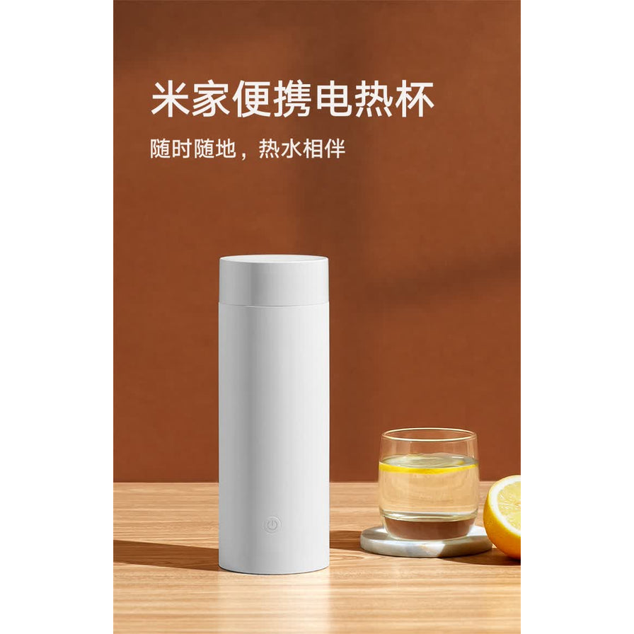 小米米家便携电热杯放置在木质桌面上，背景为暖色调，配有柠檬片和水杯，上方有文字“米家便携电热杯，随时随地，热水相伴”。