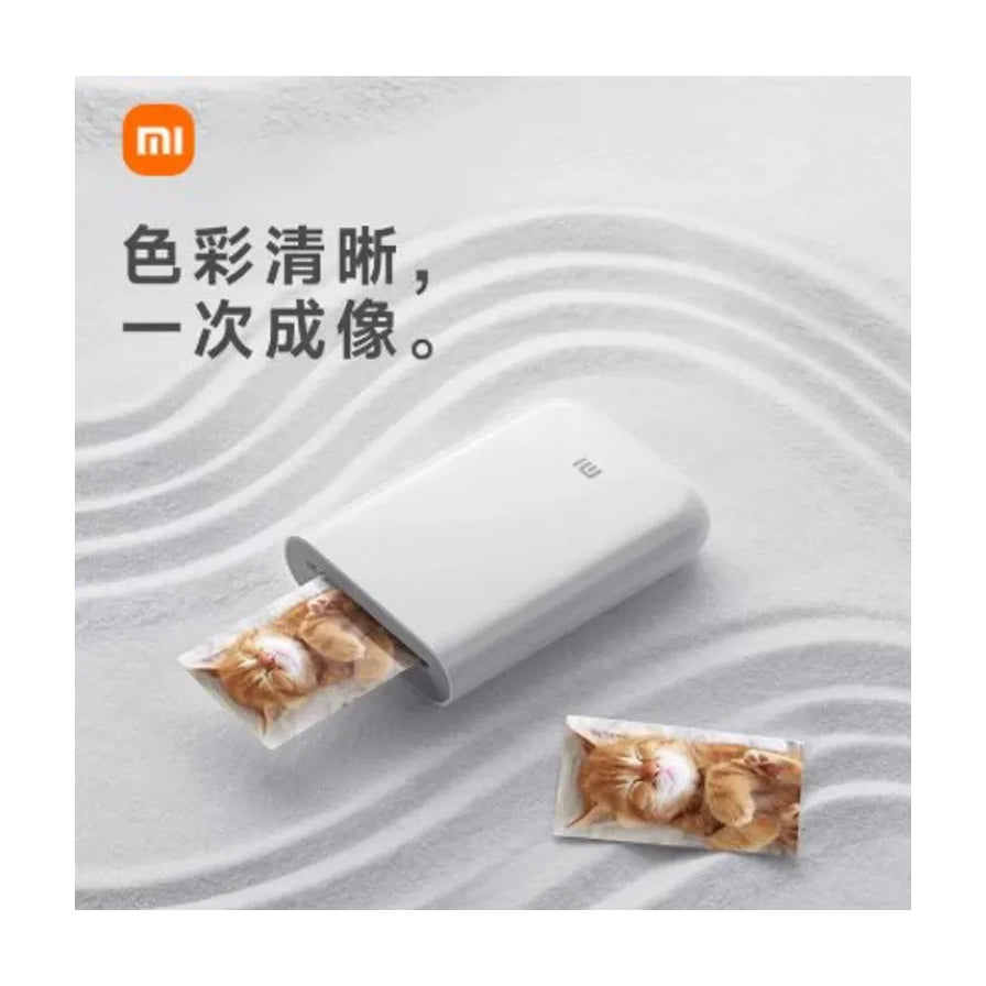 小米口袋照片打印机放置在沙纹背景上，配有小米品牌标识，上方有“色彩清晰，一次成像”的中文卖点文字。