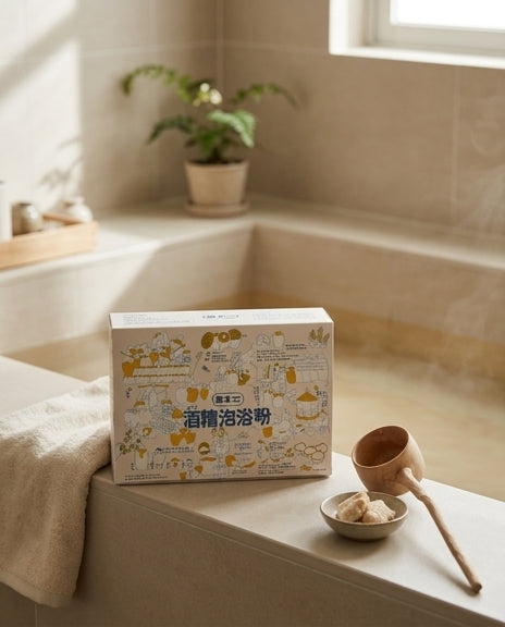 浴室场景中，真不二酒糟泡浴粉包装盒放置在浴缸边缘，旁边配有木勺和盛有粉末的小碗，背景有绿植。